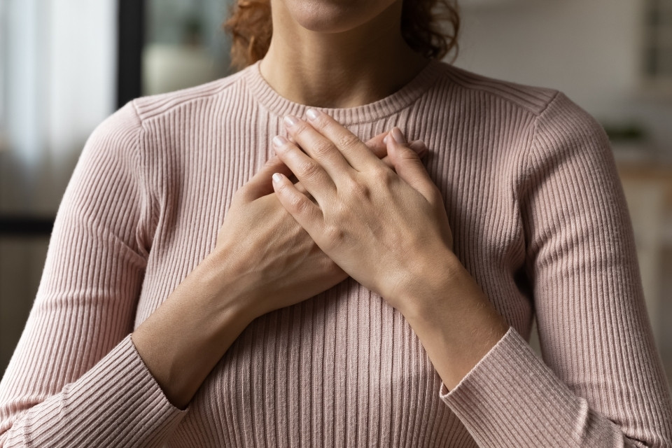 faceless woman in pink sweater with hands on top of each other placed on her chest